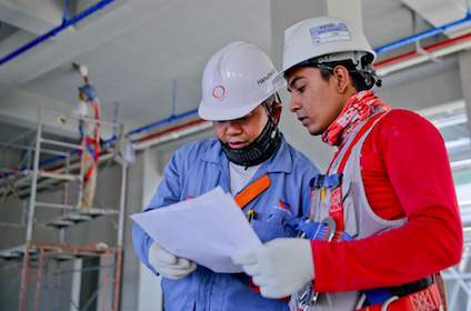 two men wearing hard hats look at a white paper together